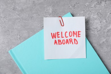 Photo of Sticky note with phrase Welcome Aboard and notebook on grey table, top view