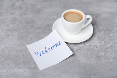 Photo of Sticky note with word Welcome and coffee on grey table, closeup