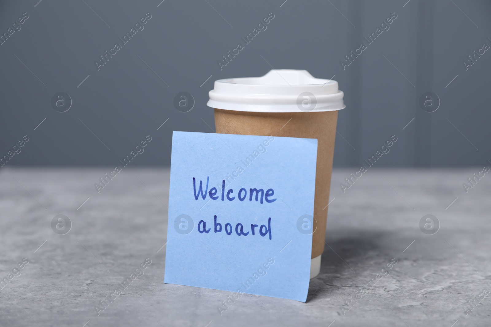 Sticky note with phrase Welcome Aboard and coffee on grey table, closeup Photo of Sticky note with phrase Welcome Aboard and coffee on grey table, closeup