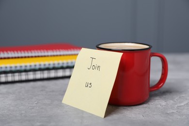 Photo of Sticky note with phrase Join Us, coffee and notebooks on grey table, closeup
