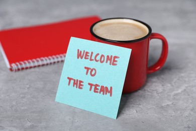 Photo of Sticky note with phrase Welcome To The Team, coffee and notebook on grey table, closeup