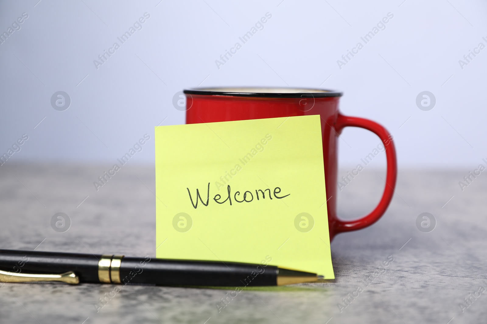 Sticky note with word Welcome, coffee and pen on grey table, closeup Photo of Sticky note with word Welcome, coffee and pen on grey table, closeup
