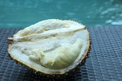 Photo of Fresh ripe durian on wicker table near swimming pool outdoors, closeup