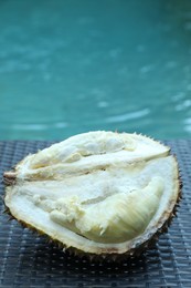 Photo of Fresh ripe durian on wicker table near swimming pool outdoors, closeup