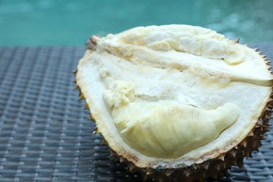 Photo of Fresh ripe durian on wicker table near swimming pool outdoors, closeup