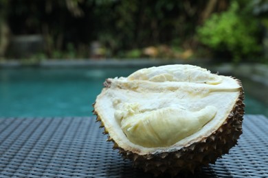 Photo of Fresh ripe durian on wicker table near swimming pool outdoors, closeup. Space for text