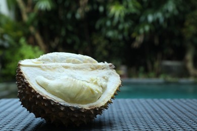 Photo of Fresh ripe durian on wicker table near swimming pool outdoors, closeup. Space for text
