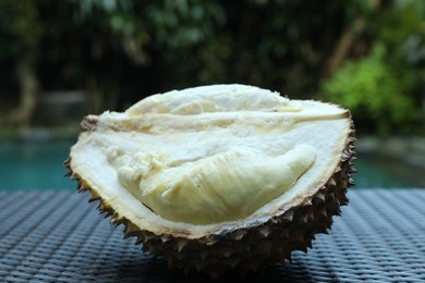 Photo of Fresh ripe durian on wicker table near swimming pool outdoors, closeup
