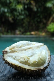 Photo of Fresh ripe durian on wicker table near swimming pool outdoors, closeup