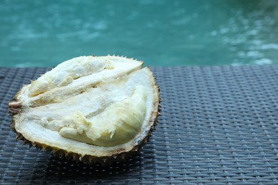 Photo of Fresh ripe durian on wicker table near swimming pool outdoors, closeup. Space for text