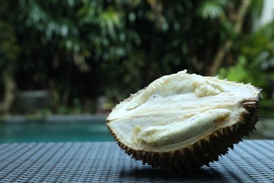 Photo of Fresh ripe durian on wicker table near swimming pool outdoors, closeup. Space for text