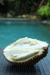 Photo of Fresh ripe durian on wicker table near swimming pool outdoors, closeup
