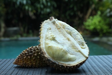 Photo of Fresh ripe durian on wicker table near swimming pool outdoors, closeup