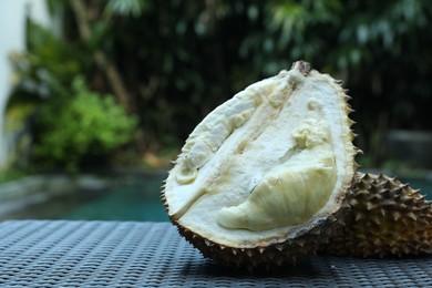 Photo of Fresh ripe durian on wicker table near swimming pool outdoors, closeup. Space for text