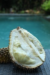 Photo of Fresh ripe durian on wicker table near swimming pool outdoors, closeup