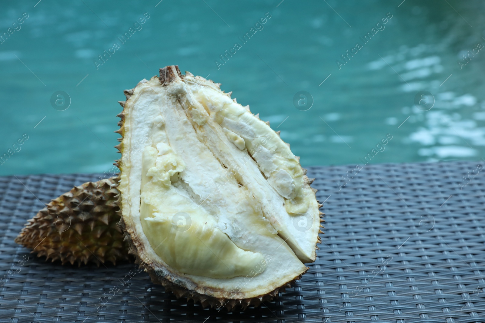 Fresh ripe durian on wicker table near swimming pool outdoors, closeup. Space for text Photo of Fresh ripe durian on wicker table near swimming pool outdoors, closeup. Space for text
