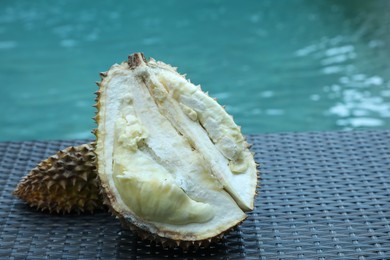 Photo of Fresh ripe durian on wicker table near swimming pool outdoors, closeup. Space for text