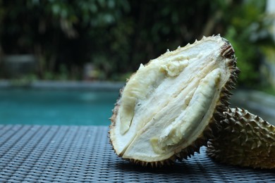 Photo of Fresh ripe durian on wicker table near swimming pool outdoors, closeup. Space for text