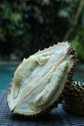 Photo of Fresh ripe durian on wicker table near swimming pool outdoors, closeup