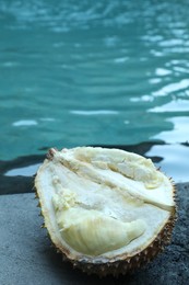 Photo of Fresh ripe durian on stone surface near swimming pool outdoors, closeup
