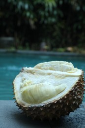 Photo of Fresh ripe durian on stone surface near swimming pool outdoors, closeup