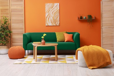 Image of Stylish living room with comfortable green sofa and bright orange wall. Interior design