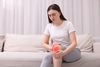 Image of Young woman suffering from pain in knee on sofa at home