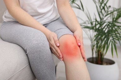Image of Woman suffering from pain in knee on sofa at home, closeup