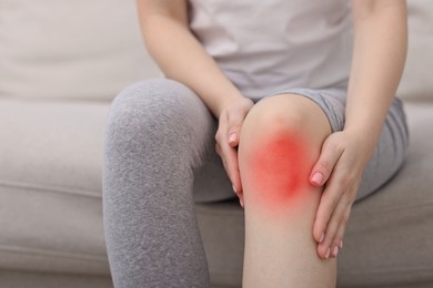 Image of Woman suffering from pain in knee on sofa at home, closeup