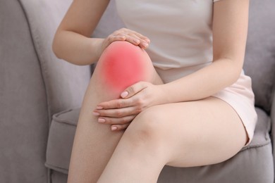 Image of Woman suffering from pain in knee on sofa at home, closeup