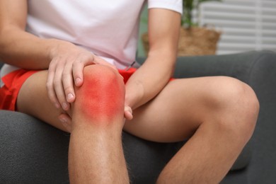 Image of Man suffering from pain in knee on sofa at home, closeup