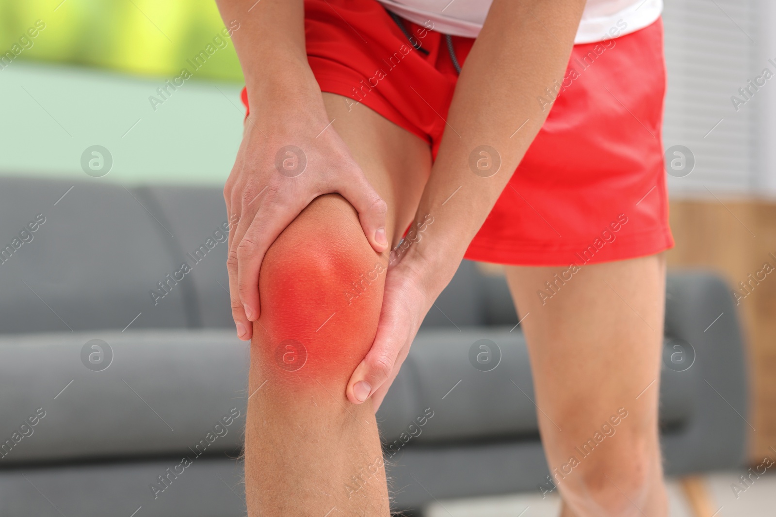 Man suffering from pain in knee at home, closeup Image of Man suffering from pain in knee at home, closeup