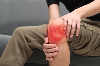 Image of Man suffering from pain in knee on sofa at home, closeup