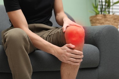 Image of Man suffering from pain in knee on sofa at home, closeup