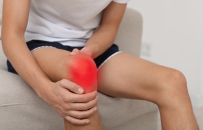 Image of Man suffering from pain in knee on sofa at home, closeup