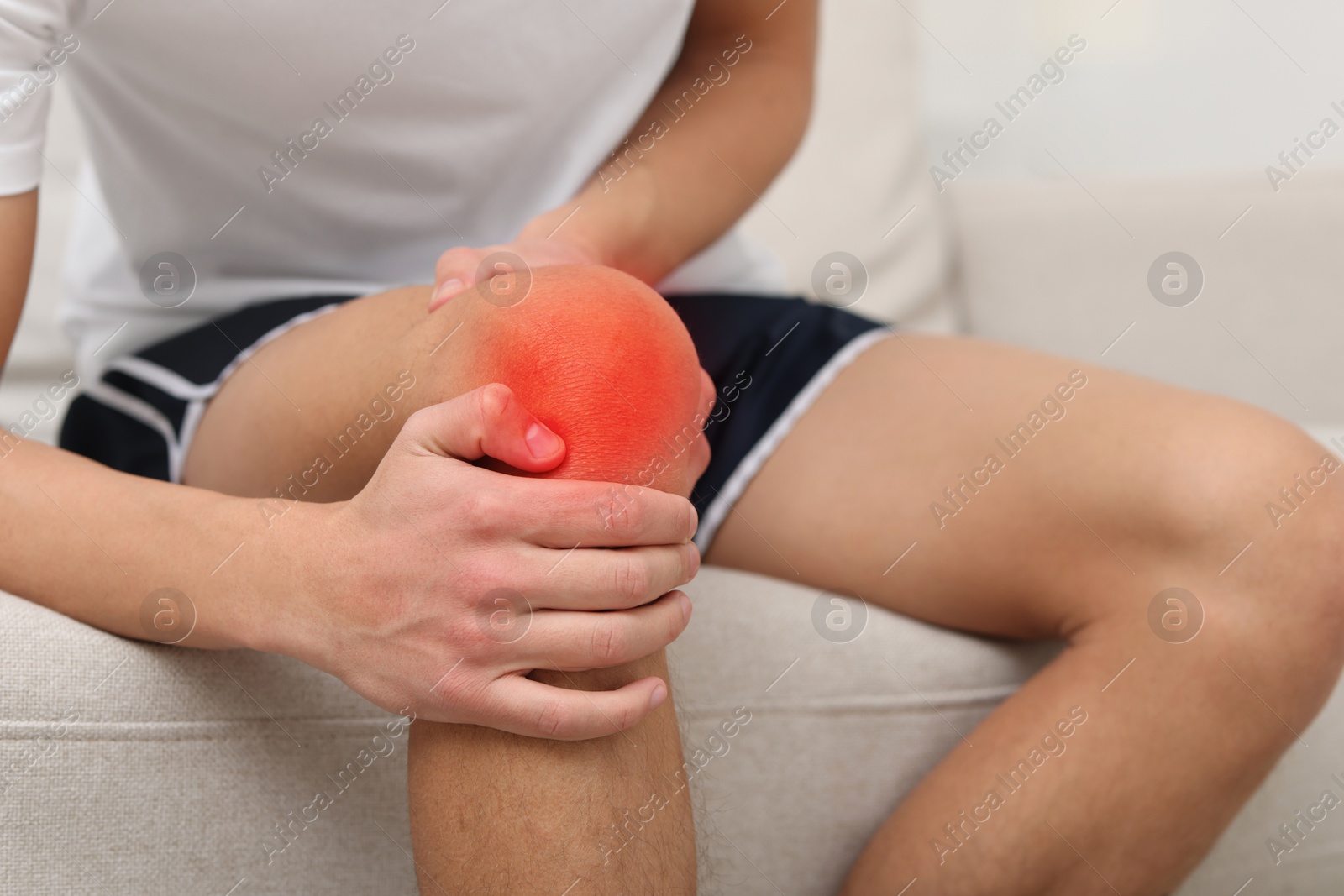 Man suffering from pain in knee on sofa at home, closeup Image of Man suffering from pain in knee on sofa at home, closeup