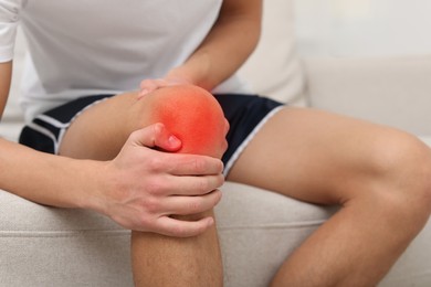 Image of Man suffering from pain in knee on sofa at home, closeup