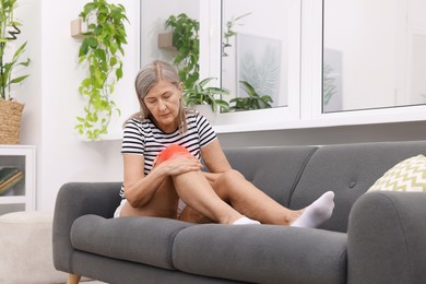 Image of Senior woman suffering from pain in knee on sofa at home