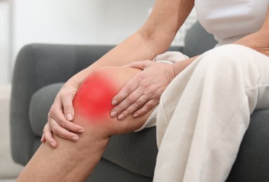 Image of Senior woman suffering from pain in knee on sofa at home, closeup