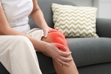 Image of Senior woman suffering from pain in knee on sofa at home, closeup