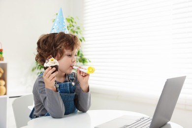 Photo of Little boy celebrating his birthday while having video call via laptop at table indoors. Space for text