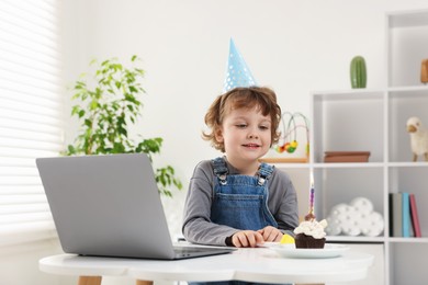 Photo of Birthday celebration. Little boy with cupcake having video call via laptop at table indoors