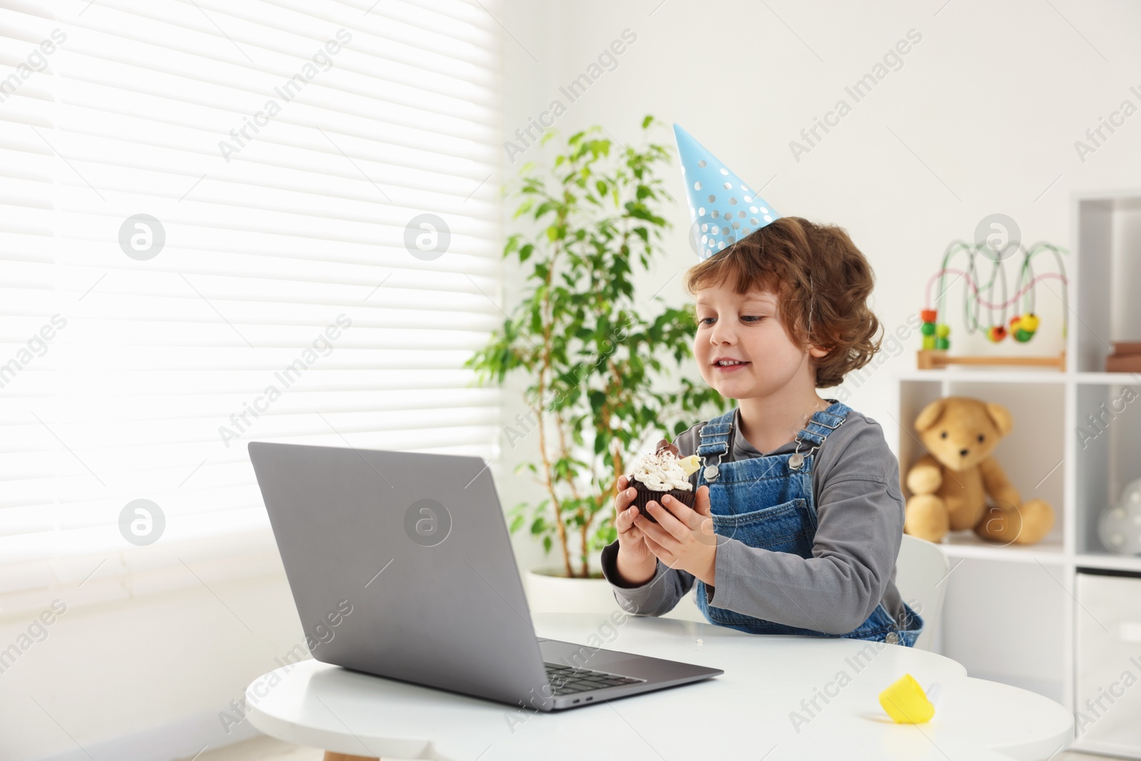 Birthday celebration. Little boy with cupcake having video call via laptop at table indoors. Space for text Photo of Birthday celebration. Little boy with cupcake having video call via laptop at table indoors. Space for text