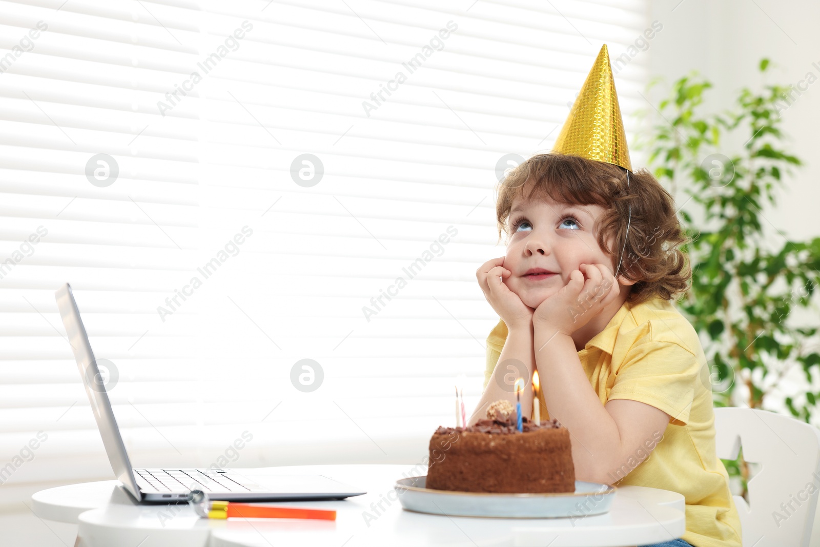 Birthday celebration. Little boy with cake making wish while having video call via laptop at table indoors. Space for text Photo of Birthday celebration. Little boy with cake making wish while having video call via laptop at table indoors. Space for text