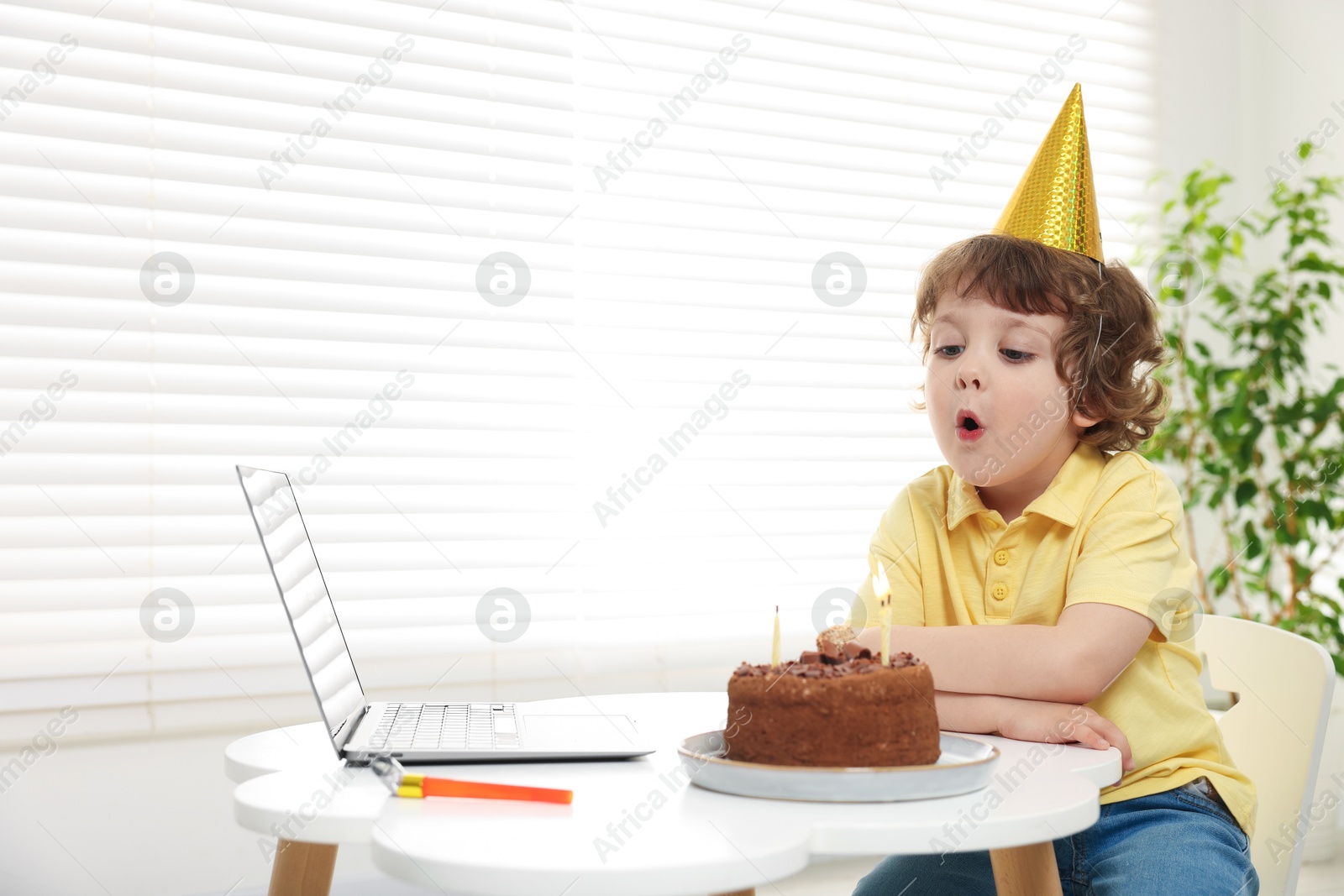 Birthday celebration. Little boy blowing candles on cake while having video call via laptop at table indoors. Space for text Photo of Birthday celebration. Little boy blowing candles on cake while having video call via laptop at table indoors. Space for text