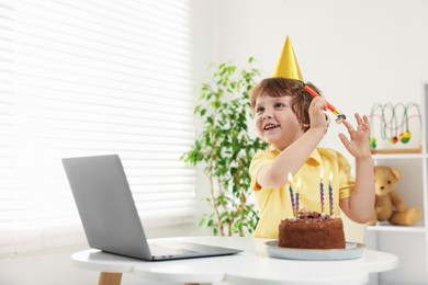 Photo of Birthday celebration. Little boy with cake having video call via laptop at table indoors. Space for text