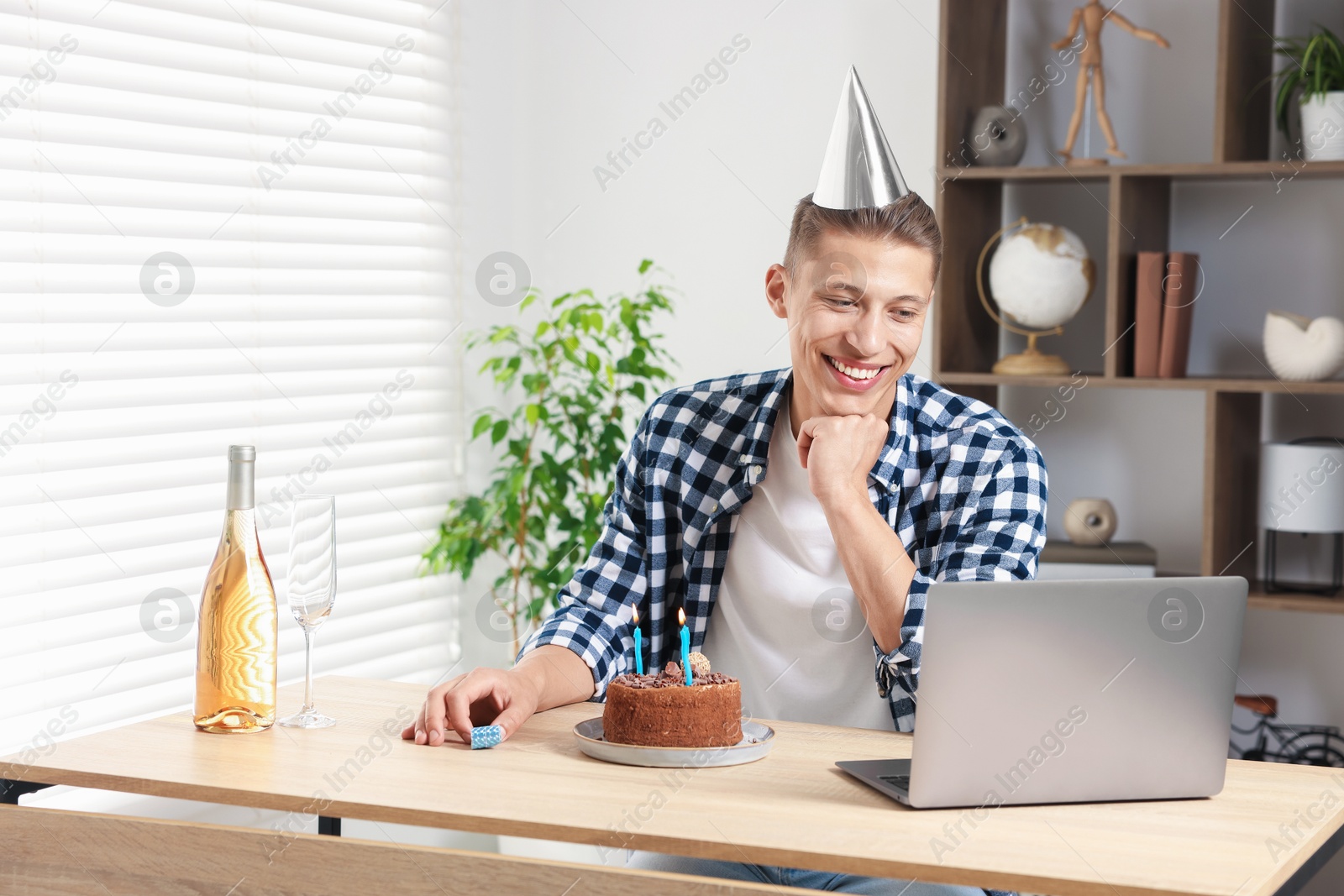 Photo of Birthday celebration. Man with cake and sparkling wine having video call via laptop at desk indoors