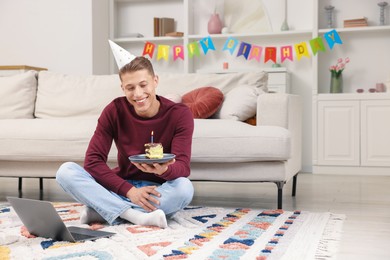 Photo of Man with piece of cake celebrating his birthday and having video call via laptop at home