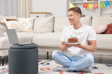 Photo of Man with cake celebrating his birthday and having video call via laptop at home