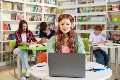 Photo of Student with laptop studying at table in library